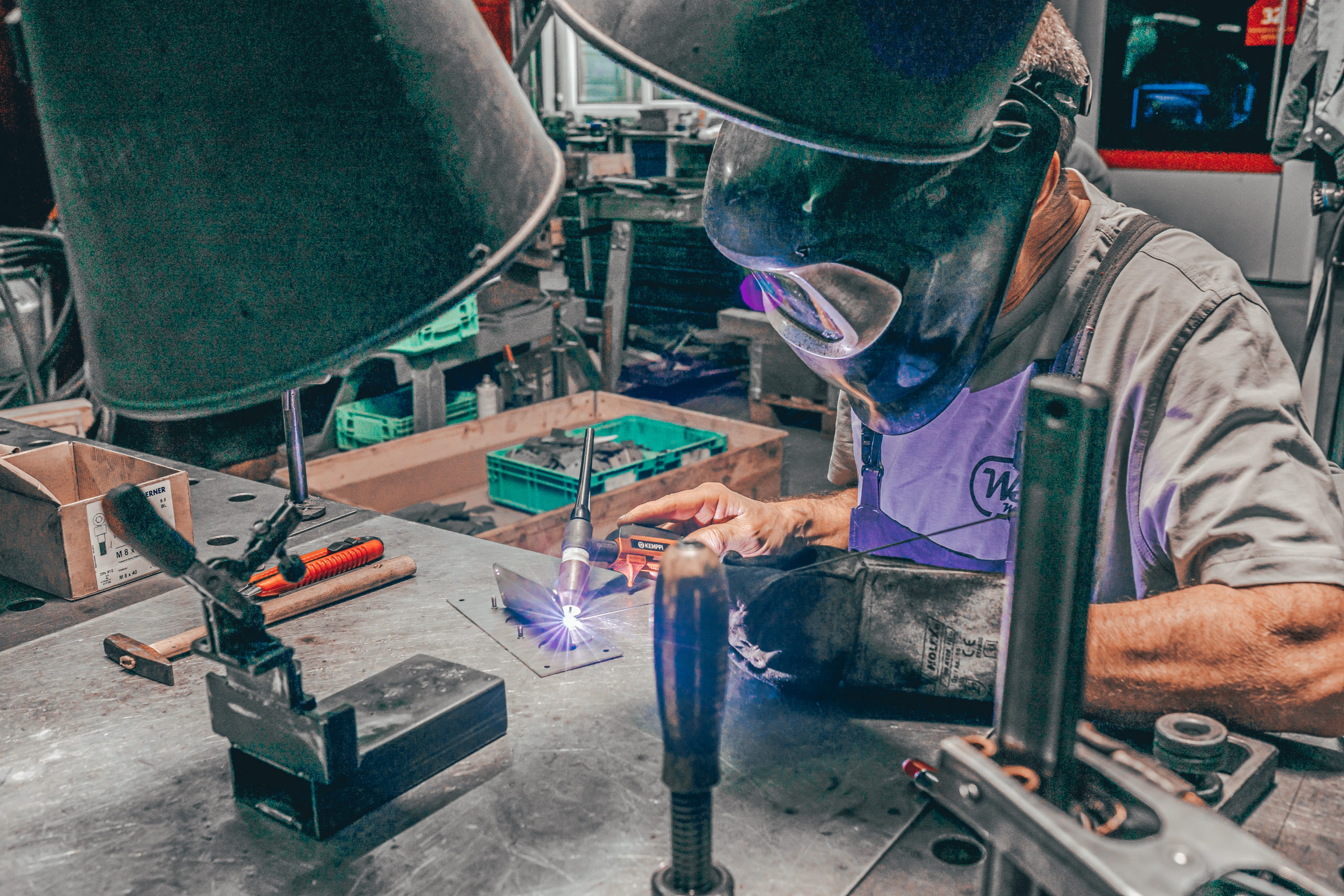 Mann in Schweißerausrüstung fertigt ein Metallteil am Arbeitsplatz