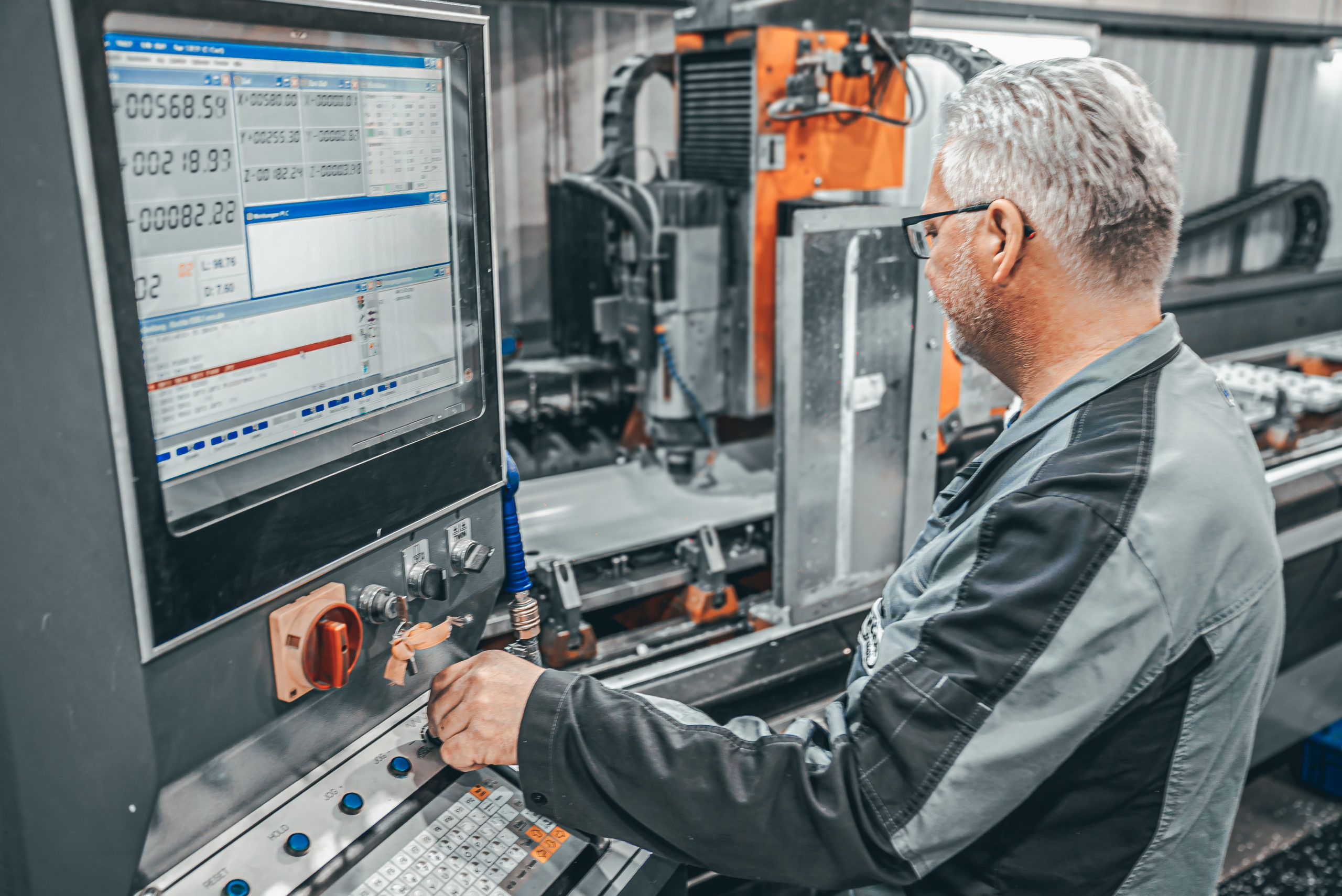 Älterer mann mit Brille und grauen Haaren stellt eine Metallverarbeitungsmaschine über einen modernen Monitor ein.